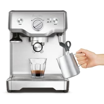 Front view of someone using the steam wand and a glass of coffee sitting on the Duo-Temp Pro.