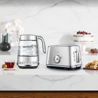 The smart crystal luxe kettle and toaster next to a cup of tea and biscuits