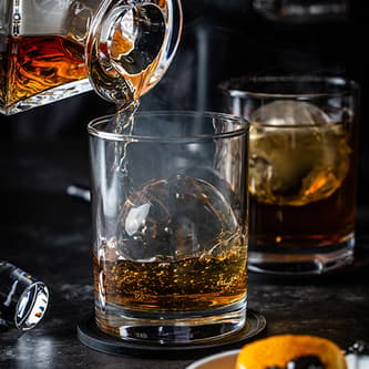 Whisky is being poured into a glass with a ball of ice.