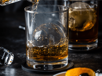 Whisky is being poured into a glass with a ball of ice.