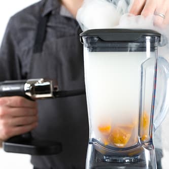 Smoke from the smoking gun fills a glass vessel with food inside.