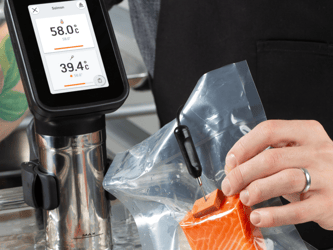 A digital needle probe that is connected to the main device is measuring the core temperature of a piece of salmon.