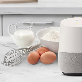 Voice device next to eggs, milk, flour and a mixer.